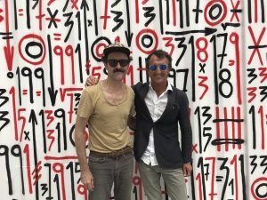 Two visitors pose in front of the Arteko Container artwork with numbers and symbols
